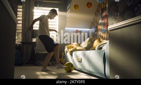 Un jeune garçon pratique le football avant le match dans sa chambre. Jeune joueur de football enthousiaste. Une salle moderne avec une guitare, des affiches sur le mur et une table d'étude avec la lampe. Banque D'Images