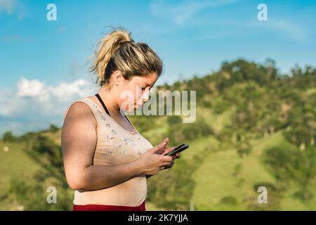 belle jeune latina femme, au sommet d'une montagne avec son téléphone portable dans la main, en interaction sur les réseaux sociaux, à la recherche d'informations avec le h Banque D'Images