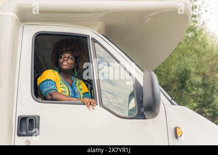 Belle femme noire aux couleurs vives assise sur le siège passager avec fenêtre vitrée cachée, offrant un air frais et une vue magnifique. Voyages et voyages. Photo de haute qualité Banque D'Images