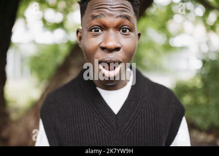 Choqué surpris jeune africain dans le parc ou la rue à l'extérieur. Automne ou printemps. Portrait gros plan Banque D'Images