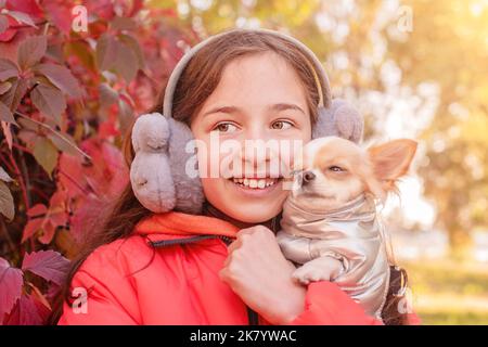 Une adolescente sourit avec un chien chihuahua dans ses bras. Une fille dans une veste orange. Banque D'Images