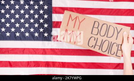 Jeune femme protestant tient le carton avec mon corps mon signe de choix contre le drapeau des États-Unis sur le fond. Fille protestant contre les lois anti-avortement. Féministe Banque D'Images