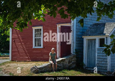 Un touriste s'assoit sur un mur de pierre de champ devant une grange rouge lors d'une journée ensoleillée à Cogswell's Grant, dans l'Essex, Massachusetts. Banque D'Images