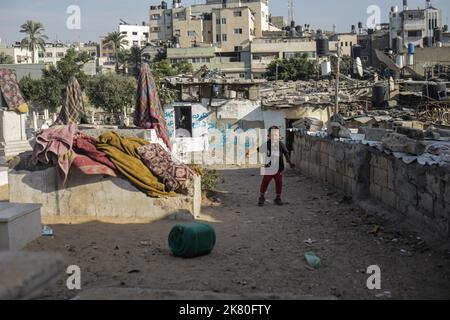 Un enfant palestinien joue devant sa maison dans le cimetière Sheikh Shaban de la ville de Gaza. Taux de chômage élevés et manque de possibilités d'emploi à Gaza, et nombre croissant de familles confrontées à la pauvreté après avoir perdu un emploi au cours des dix dernières années du blocus de Gaza. Une bataille pour l'espace entre les vivants et les morts fait rage alors que les sans-abri s'installent dans les cimetières de la région tandis que les autorités sont aux prises avec la demande croissante de nouveaux logements. Kahil a dit: Si les morts parlaient, ils nous diraient de sortir d'ici. Qui vivait dans le cimetière du centre de Gaza avec son mari et une famille de six non Banque D'Images