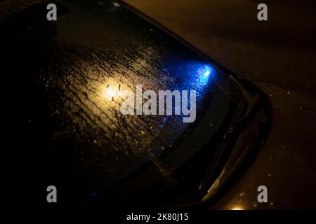 Signal bleu sous la vitre de la voiture. Témoin lumineux sous vitre humide. Détails du transport de nuit. Voiture humide dans le parking. Banque D'Images