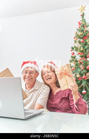 Un couple latin senior a accueilli ses proches par appel vidéo à Noël, leur montrant leurs cadeaux. Concepts: La joie de partager pendant les vacances, le Banque D'Images