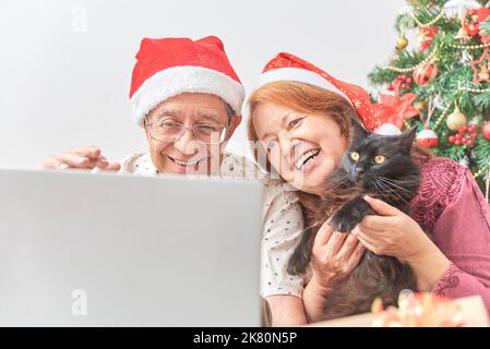 Un couple senior et un chat saluent leurs proches par appel vidéo à Noël. Concepts: animaux de compagnie en tant que partie de la famille, la joie de partager pendant les vacances, Banque D'Images