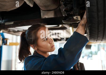 La résolution de problèmes est une grande partie du travail. Une femme mécanicien travaillant sous une voiture soulevée. Banque D'Images