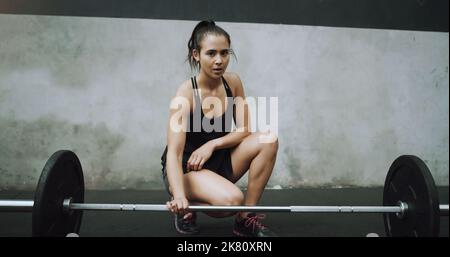 J'ai des poids à soulever et des objectifs à atteindre. Portrait d'une jeune femme s'exerçant avec une barbell dans une salle de gym. Banque D'Images