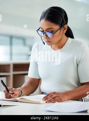 Je ne me suis jamais reculée. Une jeune femme d'affaires attirante assise seule dans son bureau et écrivant des notes tout en portant un casque. Banque D'Images