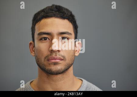 Je m'efforce de cacher mes sentiments. Un beau jeune homme debout sur fond gris. Banque D'Images