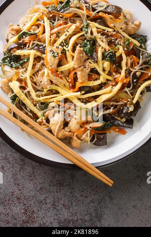 Japchae Korean Glass Noodle faire frire avec des œufs, des légumes et des champignons, sur l'assiette de la table. Vue verticale du dessus Banque D'Images