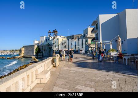 Touristes marchant le long du front de mer d'Otrante sur Lungomare degli Eroi (la promenade des héros) dans le soleil de l'après-midi. Pouilles (Puglia), Italie. Banque D'Images