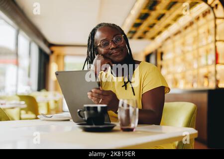 Femme d'affaires mature regardant la caméra tout en tenant une tablette numérique dans un café. Femme indépendante senior faisant un certain travail indépendant en ligne dans un Banque D'Images