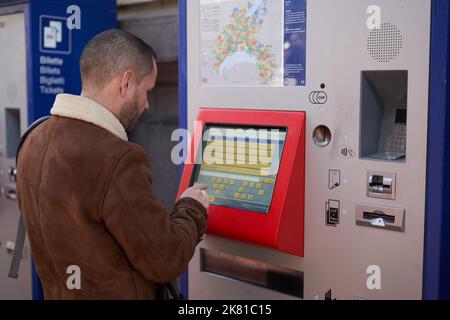 Un touriste de race blanche achetant un billet à un terminal rouge sur fond flou Banque D'Images