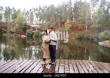Le couple heureux voyage en automne dans un endroit pittoresque au milieu des rochers et de l'eau. Recouvert d'une couverture de pluie. Soft focus .Ukraine, carrière de Korostyshiv. Banque D'Images