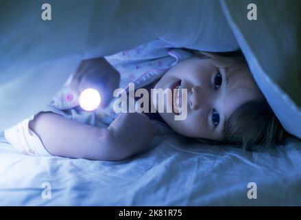 Jeune fille sous couverture avec lumière dans le lit la nuit Banque D'Images