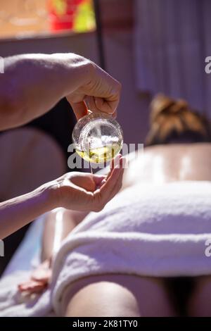 Goias, Brésil – 01 octobre 2022 : massothérapeute versant de l'huile sur les mains avec un patient allongé sur une civière en arrière-plan. Banque D'Images