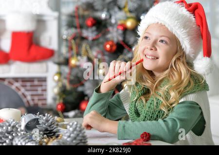 Petite fille écrivant la lettre à santa dans chapeau de santa à homer Banque D'Images