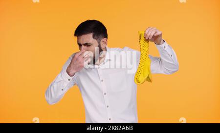 mécontent homme en chemise blanche tenant des chaussettes stinky tout en bouchant le nez isolé sur jaune Banque D'Images