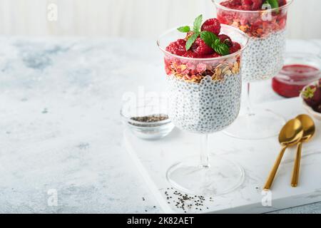 Pudding au Chia. Pudding sain au chia de vanille dans un verre avec des framboises fraîches et de la menthe sur fond blanc. Petit déjeuner sain végétalien. Banque D'Images