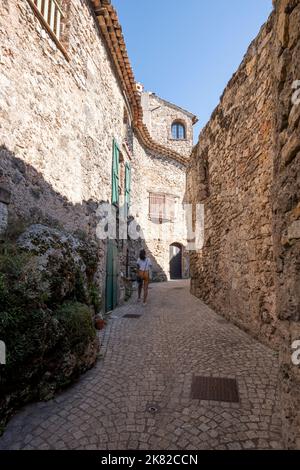 Une dame touristique marchant dans une rue de Tourtour avec des maisons en pierre surmontée de tuiles rondes, un village très touristique dans le sud de la France. Banque D'Images