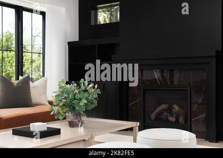 Un salon confortable avec un canapé en cuir et une table en bois devant une étagère et une cheminée noires intégrées. Banque D'Images