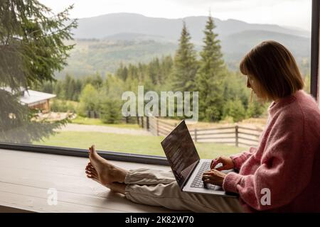 Femme travaille sur ordinateur portable à la maison dans les montagnes Banque D'Images