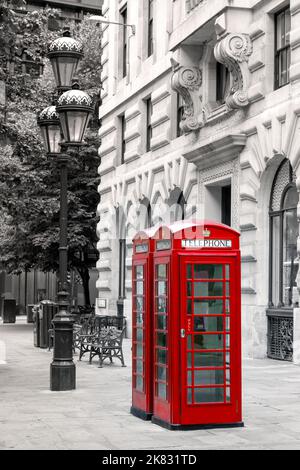 Boîtiers de téléphone rouge vif sur une rue de ville avec lampadaire, bancs et arbres en arrière-plan. Noir et blanc avec les cabines téléphoniques choisies o Banque D'Images