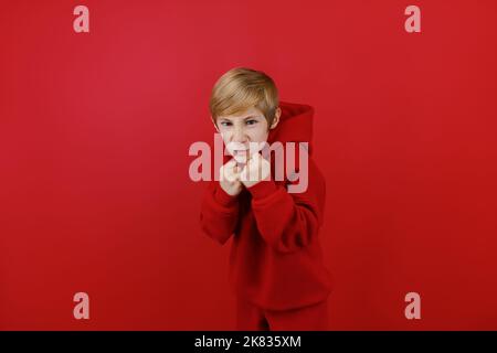 un garçon dans un tracksuit rouge a serré ses poings et les a mis en avant Banque D'Images