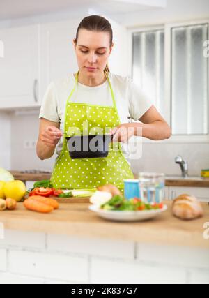 Jeune femme de ménage mélangeant la vinaigrette dans une casserole dans la cuisine maison Banque D'Images