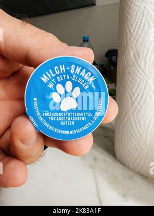 Paris, France - 13 septembre 2022: POV main mâle tenant Milch-snack avec bêta glucan nourriture pour chats - cuisine moderne fond se préparant à nourrir l'animal de chat Banque D'Images