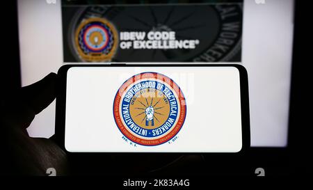 Personne tenant un téléphone mobile avec le logo du syndicat nord-américain IBEW sur l'écran en face de la page Web. Mise au point sur l'affichage du téléphone. Banque D'Images