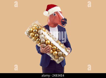 Homme en costume, chapeau de Noël et masque de cheval amusant tenant un grand ensemble de boules d'arbre de Noël Banque D'Images