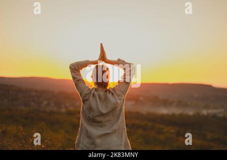 Vue arrière de la femme avec les bras dans le namaste au-dessus de la colline au coucher du soleil Banque D'Images