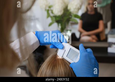 Le médecin examine la peau de la tête de la jeune femme avec un système d'équipement de dermatologie spécial, la perte de cheveux et le concept de trichologie. Analyse des cheveux avec analyse Banque D'Images