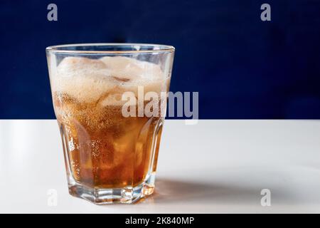Un verre de cola avec de la glace sur une table blanche en gros plan. Boisson rafraîchissante froide Banque D'Images