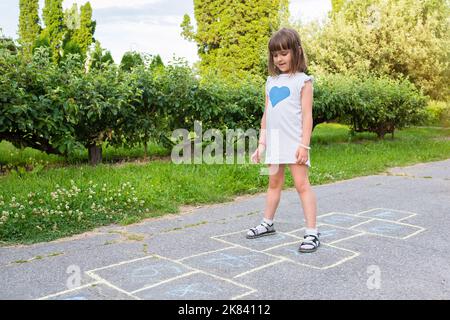 Un enfant mignon sur le trottoir attire et joue à des jeux pour enfants Banque D'Images