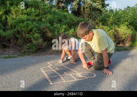 Les enfants s'attirent dans la craie sur la chaussée, dans le parc au coucher du soleil Banque D'Images