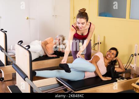 Femme hispanique pratiquant le pilates sur réformateur avec une jeune femme entraîneur Banque D'Images