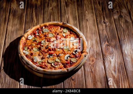 Pizza appétissante avec saucisses de chasse, mozzarella, concombres marinés, piments à base de tomate sur fond de bois. Banque D'Images