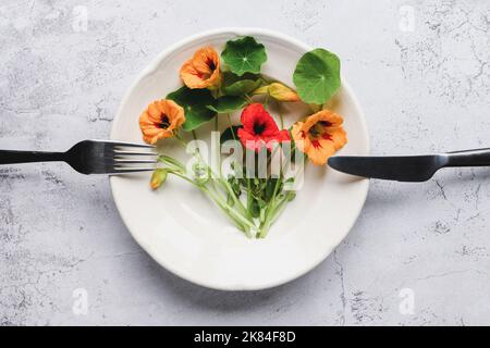 Plantes de Naturtium, fleurs de cresson indiennes et feuilles dans l'assiette sur la table de cuisine, vue du dessus Banque D'Images