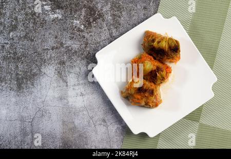 Rouleaux de chou farcis avec de la viande et du riz sur une assiette carrée blanche sur fond sombre. Vue de dessus, plan d'appartement Banque D'Images