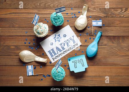 Carte avec texte HAPPY INDEPENDENCE DAY, note avec numéro 74 et cupcakes sur fond en bois Banque D'Images