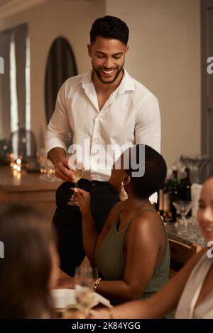 Voilà, c'est beau. Un beau jeune homme qui donne à son ami un verre de champagne lors d'un dîner. Banque D'Images