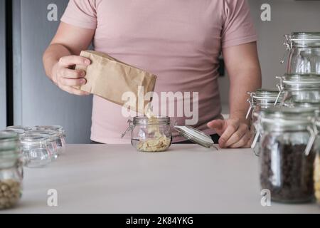 Homme méconnaissable remplissant un pot d'amandes blanchies en tranches dans un sac en papier. Banque D'Images