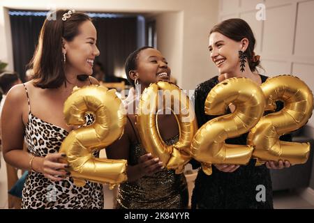 Étaient prêts pour le nouvel an. Un groupe diversifié d'amis debout ensemble et tenant 2022 ballons pendant un dîner du nouvel an. Banque D'Images