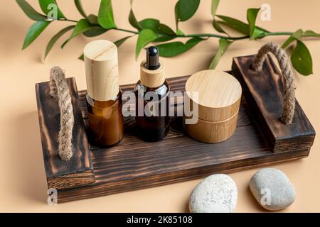 Maquette de la marque du SPA cosmétique. Bouteilles et bocaux cosmétiques en verre foncé avec plateau en bois sur fond beige. Concept de produit de beauté naturel biologique, M Banque D'Images