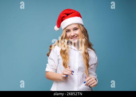 Fille de Noël. Magnifique modèle ado en chapeau de santa isolé sur fond en studio. Drôle de rire surpris portrait de jeune femme. Émotions réelles. Concept des ventes de noël et du nouvel an Banque D'Images