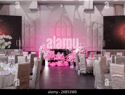 Vue générale sur le présidium de mariage, mis en évidence par un ton violet dans la salle de restaurant, au milieu des tables de banquet et des écrans numériques. Banque D'Images